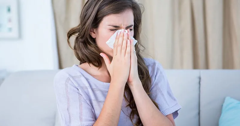 Woman sneezing into a tissue from allergies