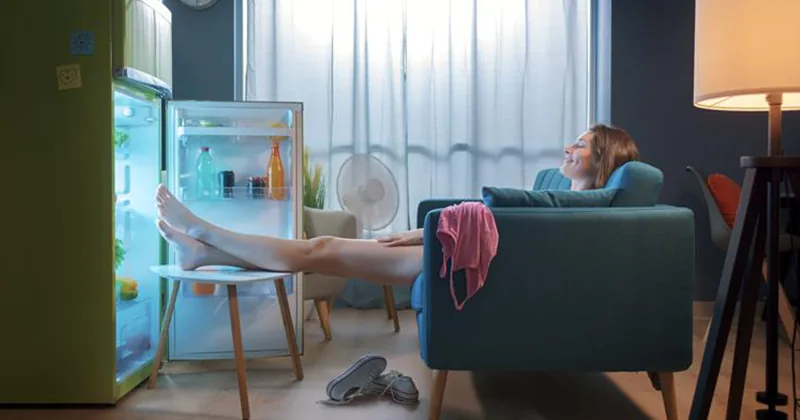 Person cooling off in front of an open fridge because the AC isn't keeping up
